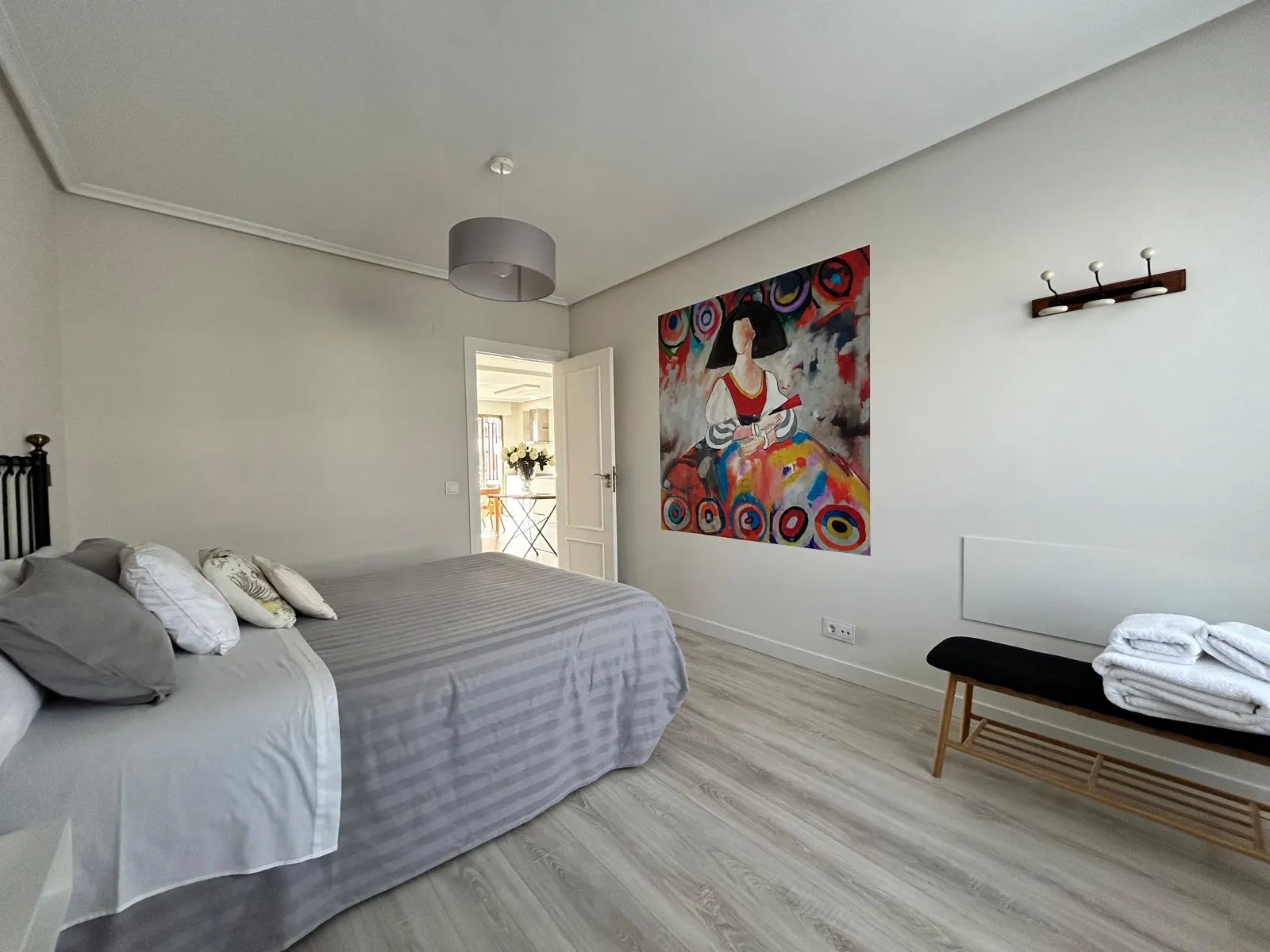 Dormitorio con banco a los pies de la cama y cuadro de colores